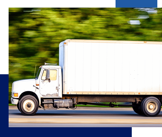 A white truck driving down the road near trees.